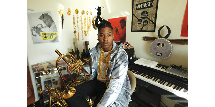 Christian Scott aTunde Adjuah sits in a room full of instruments and art. 